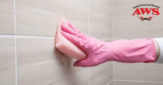 hand in glove cleaning bathroom wall with sponge
