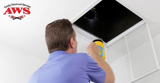 man looking into vent with flashlight